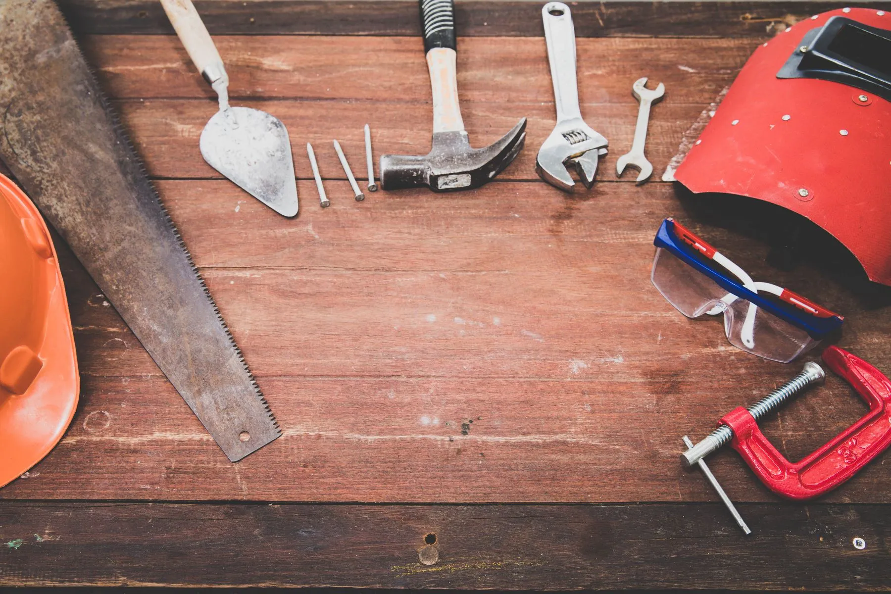 Herramientas sobre una mesa de madera: martillo, llaves, cuchara de albañil y casco
