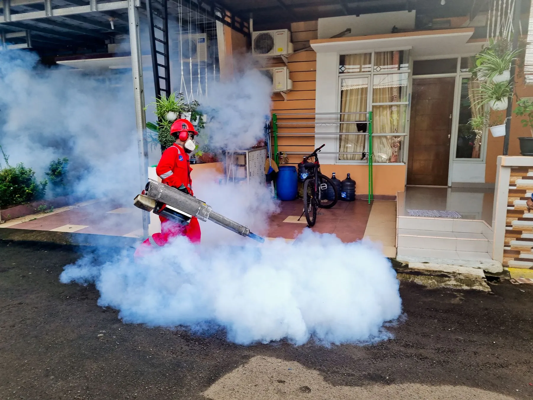 Técnico con equipo de protección termonebulizando frente a una casa