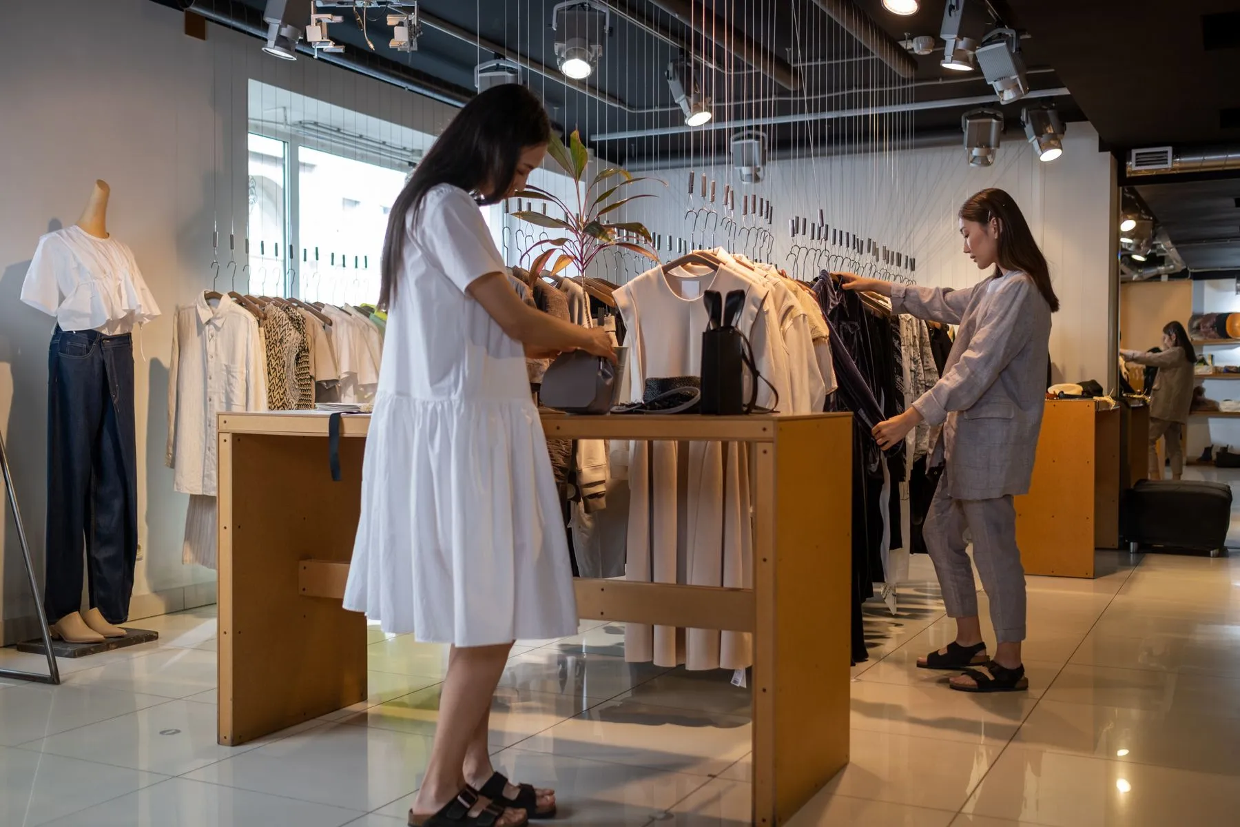 Clientas mirando ropa en los percheros de una tienda luminosa