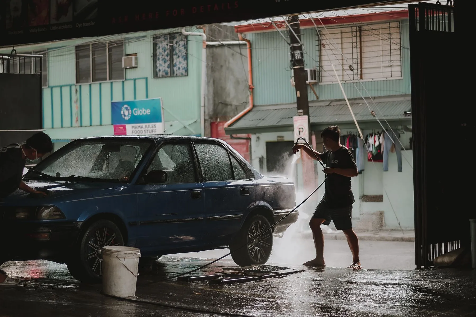Hombre lavando un auto con manguera frente al lavadero