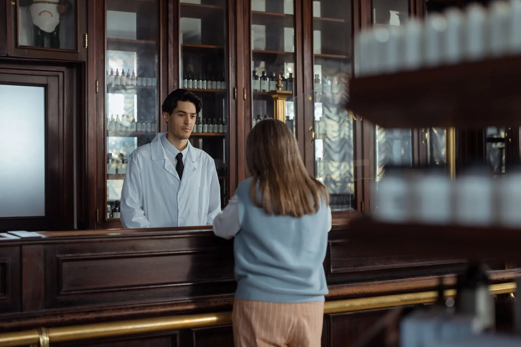 Farmacéutico atendiendo a una clienta en el mostrador de la farmacia