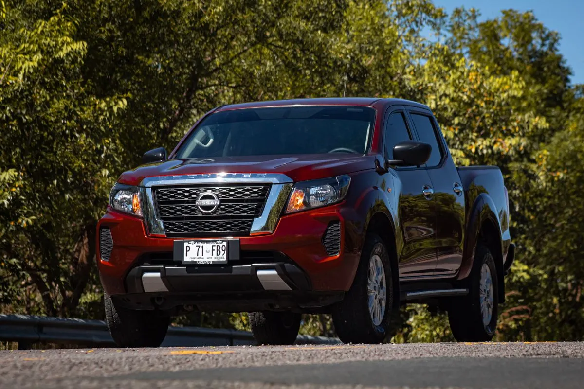 Camioneta Nissan Frontier doble cabina roja estacionada entre árboles