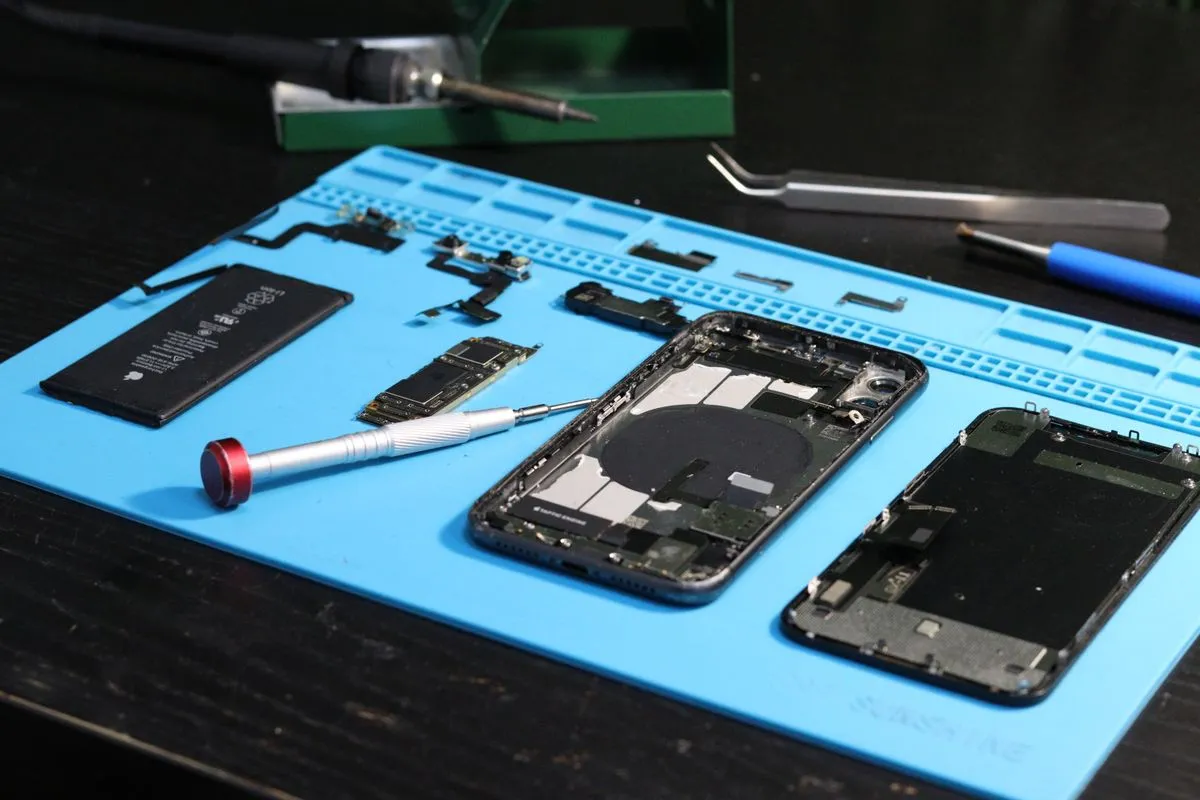 Celular desarmado con sus piezas y herramientas sobre una alfombra de reparación