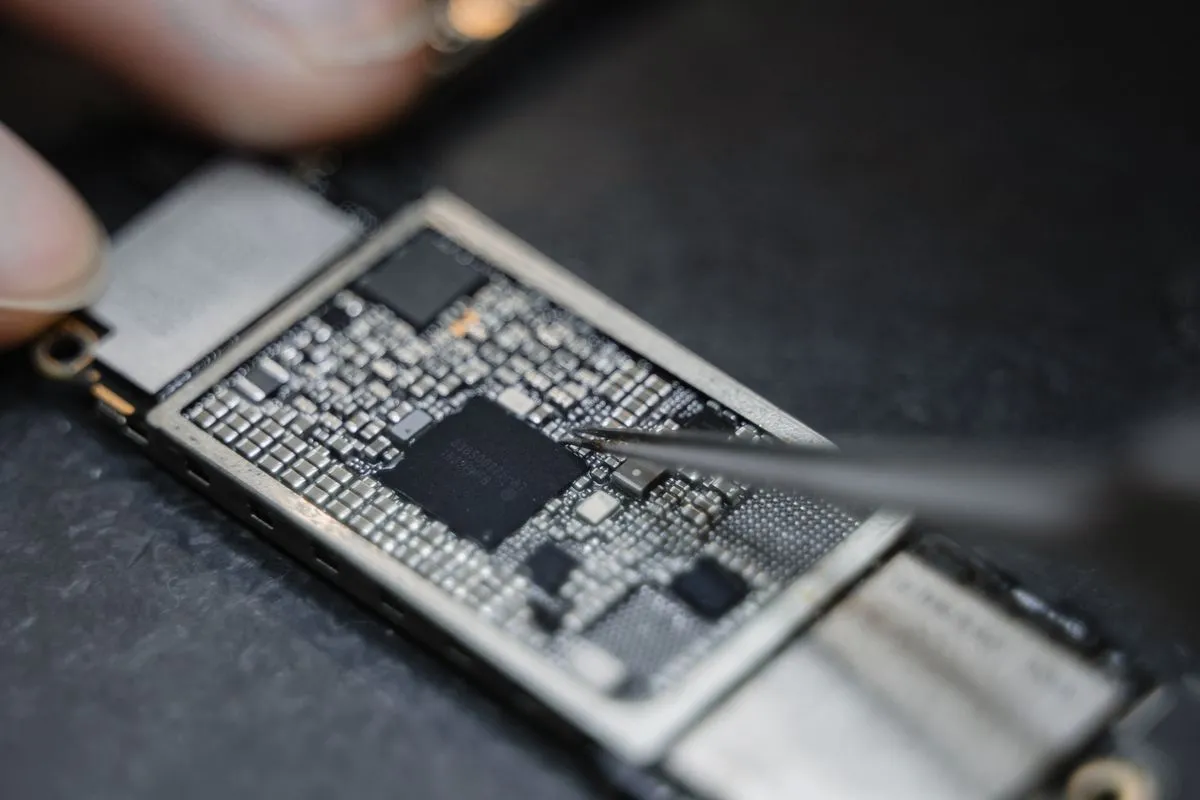 Técnico trabajando con pinza sobre la placa de un celular