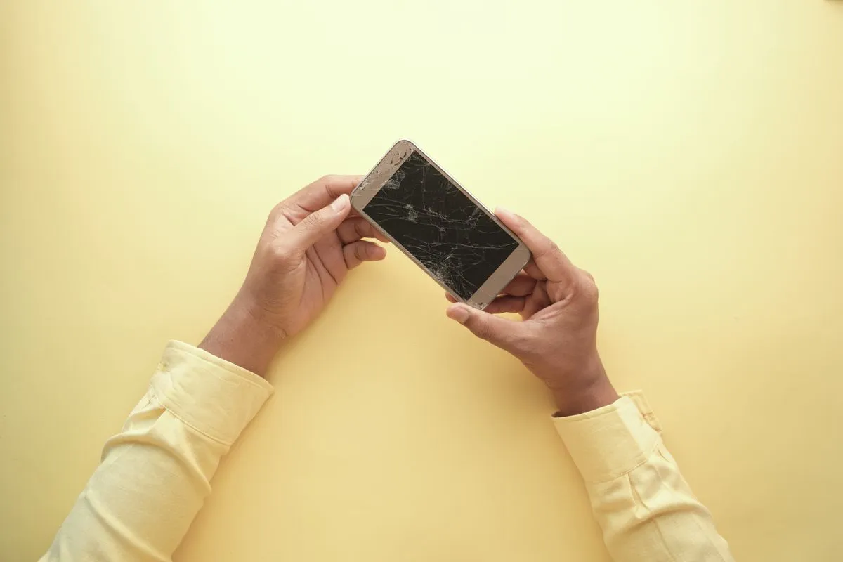 Manos sosteniendo un celular con la pantalla rota