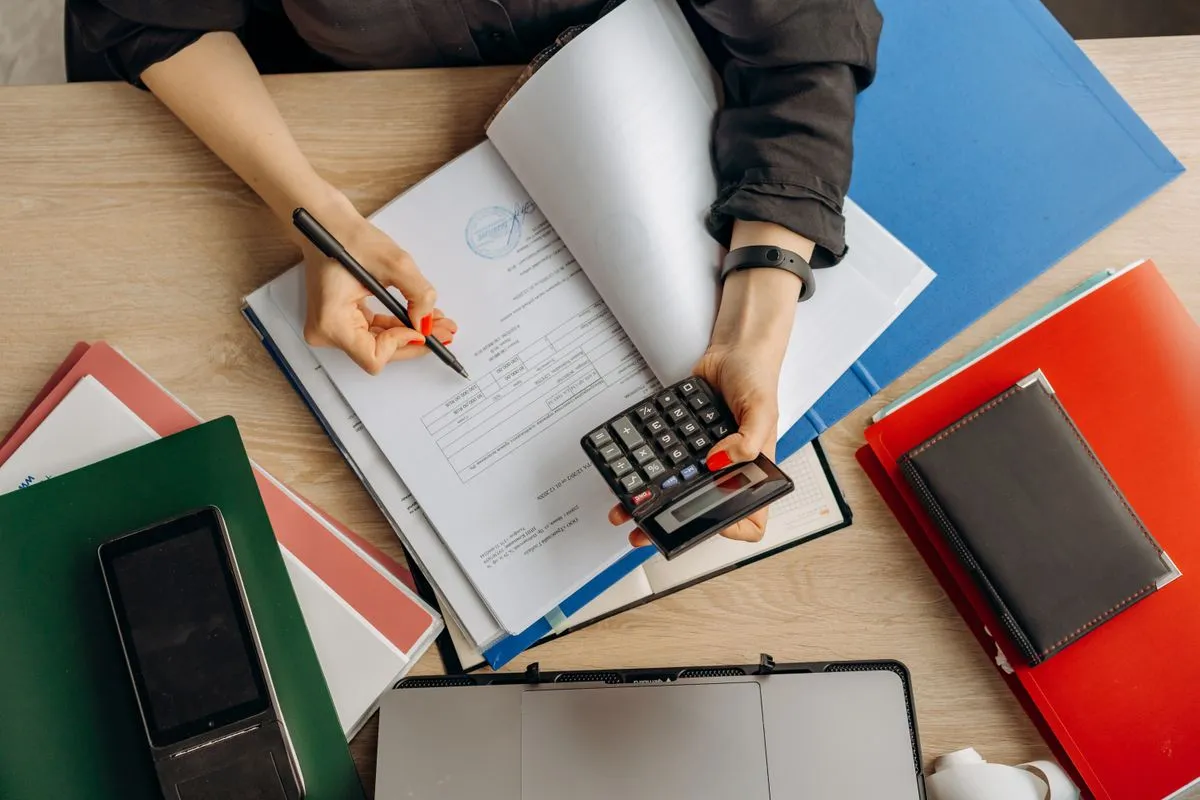 Manos con calculadora y bolígrafo sobre documentos y carpetas
