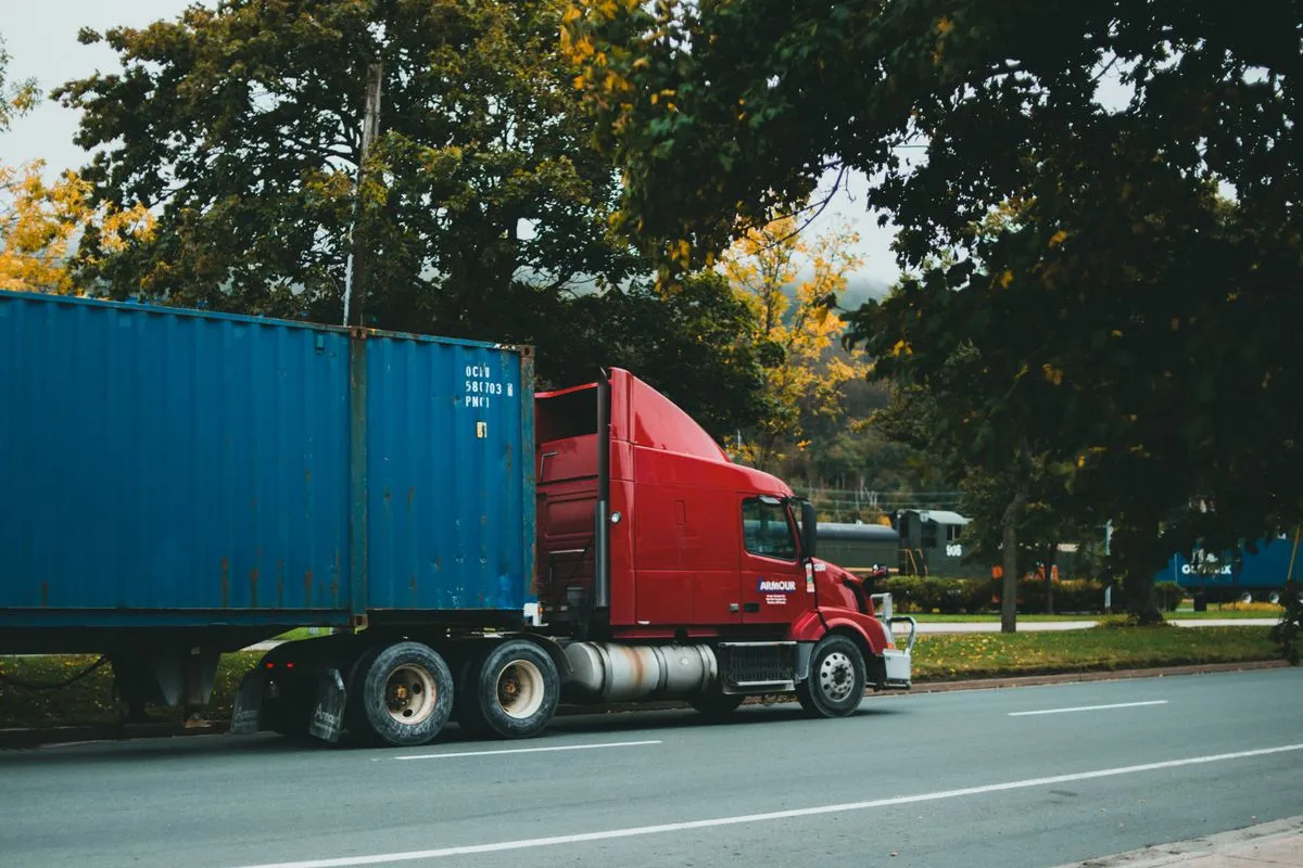 Camión rojo llevando un contenedor azul por una ruta arbolada