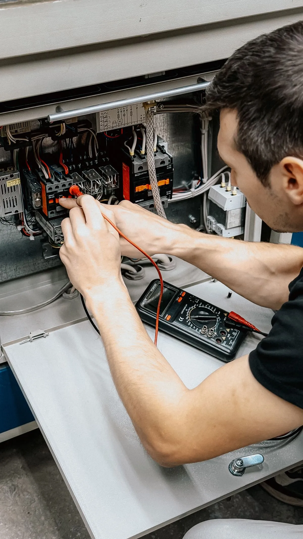 Electricista midiendo con multímetro dentro de un tablero abierto