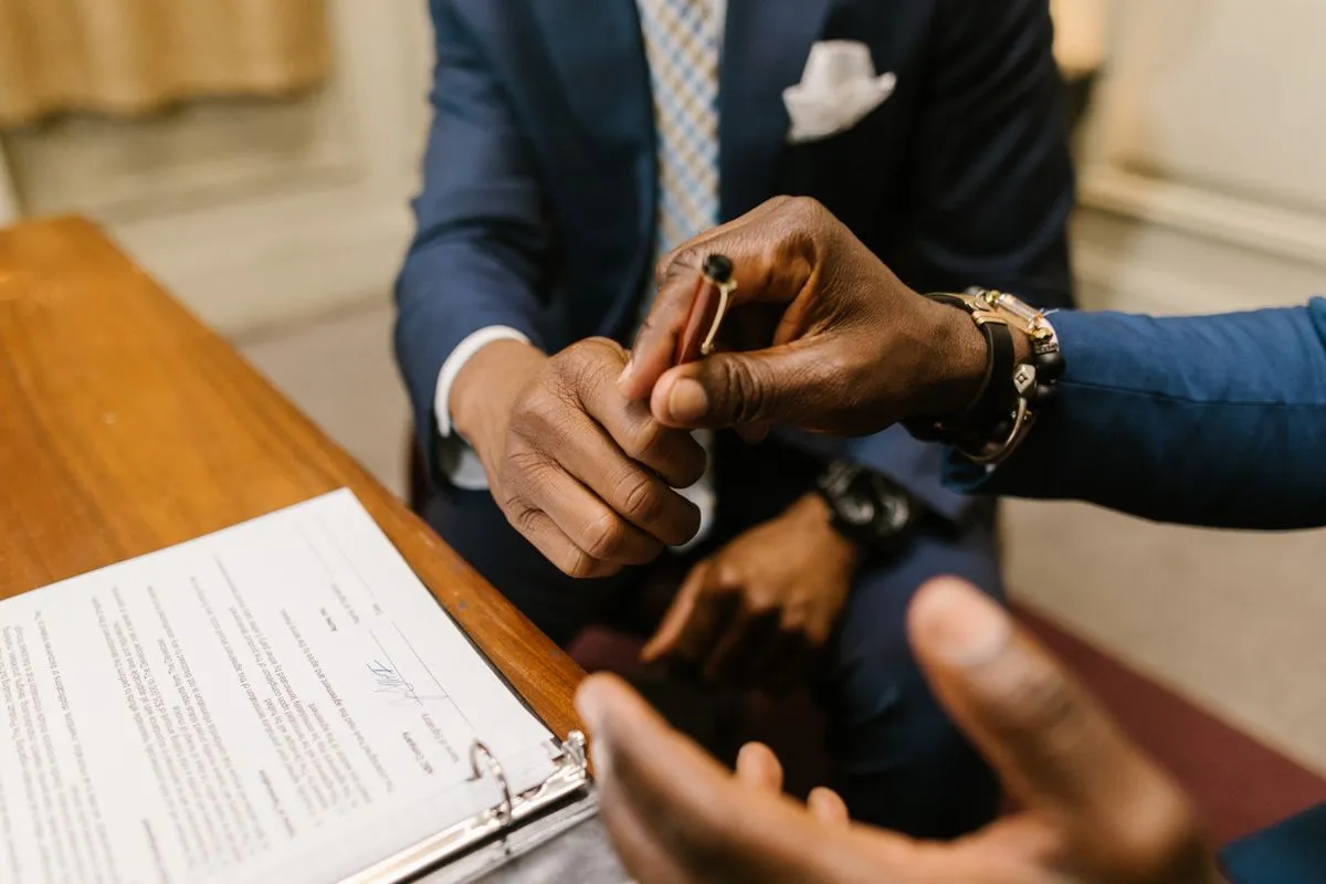 Dos personas de traje pasándose la lapicera para firmar un contrato