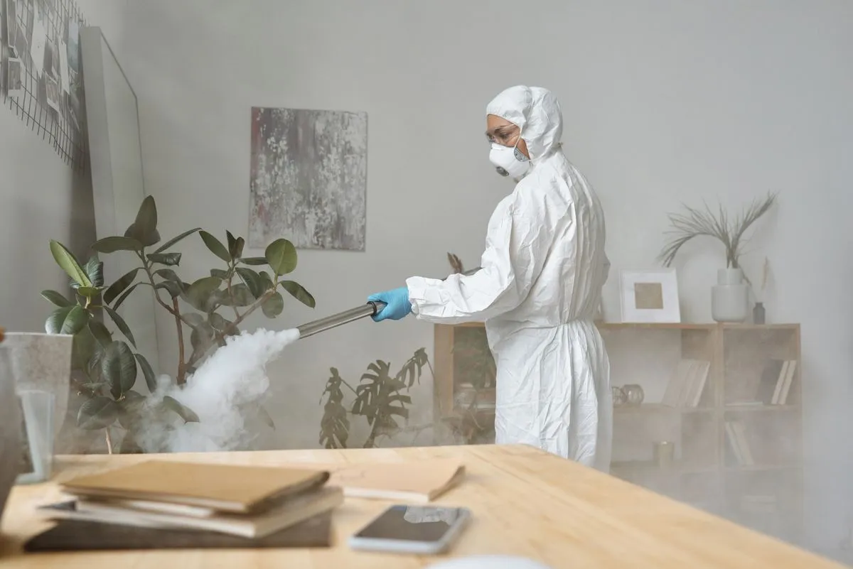 Técnico con traje de protección fumigando una sala con plantas