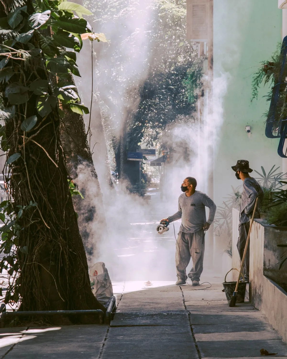Dos trabajadores fumigando una vereda con niebla