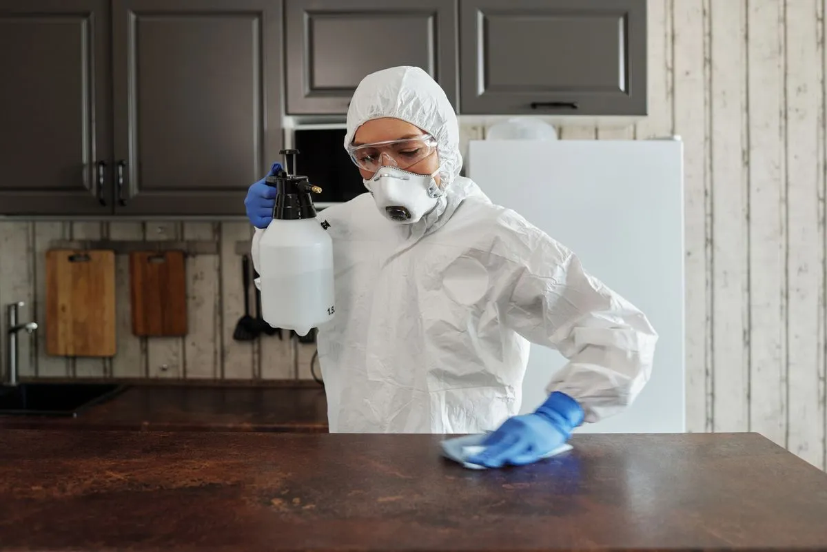 Técnica con protección desinfectando la mesada de una cocina
