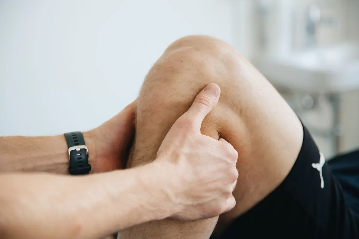 Manos de un kinesiólogo trabajando sobre la rodilla de un paciente