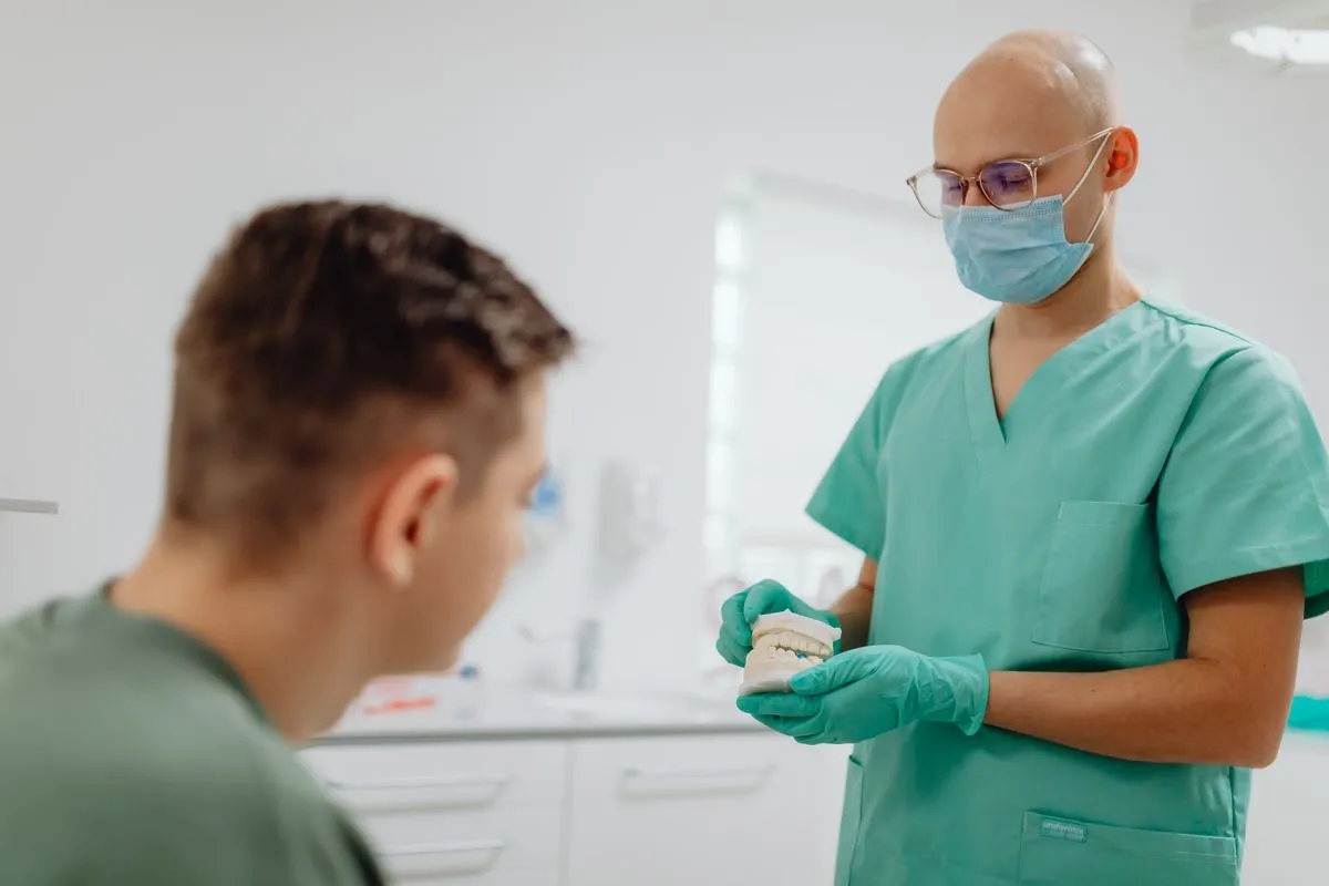 Odontólogo explicándole el tratamiento a un paciente con un modelo dental