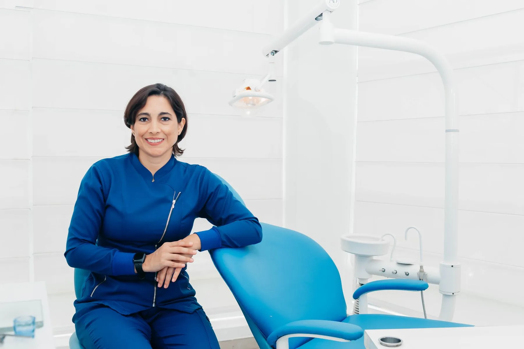 Odontóloga sonriente sentada junto al sillón en un consultorio luminoso