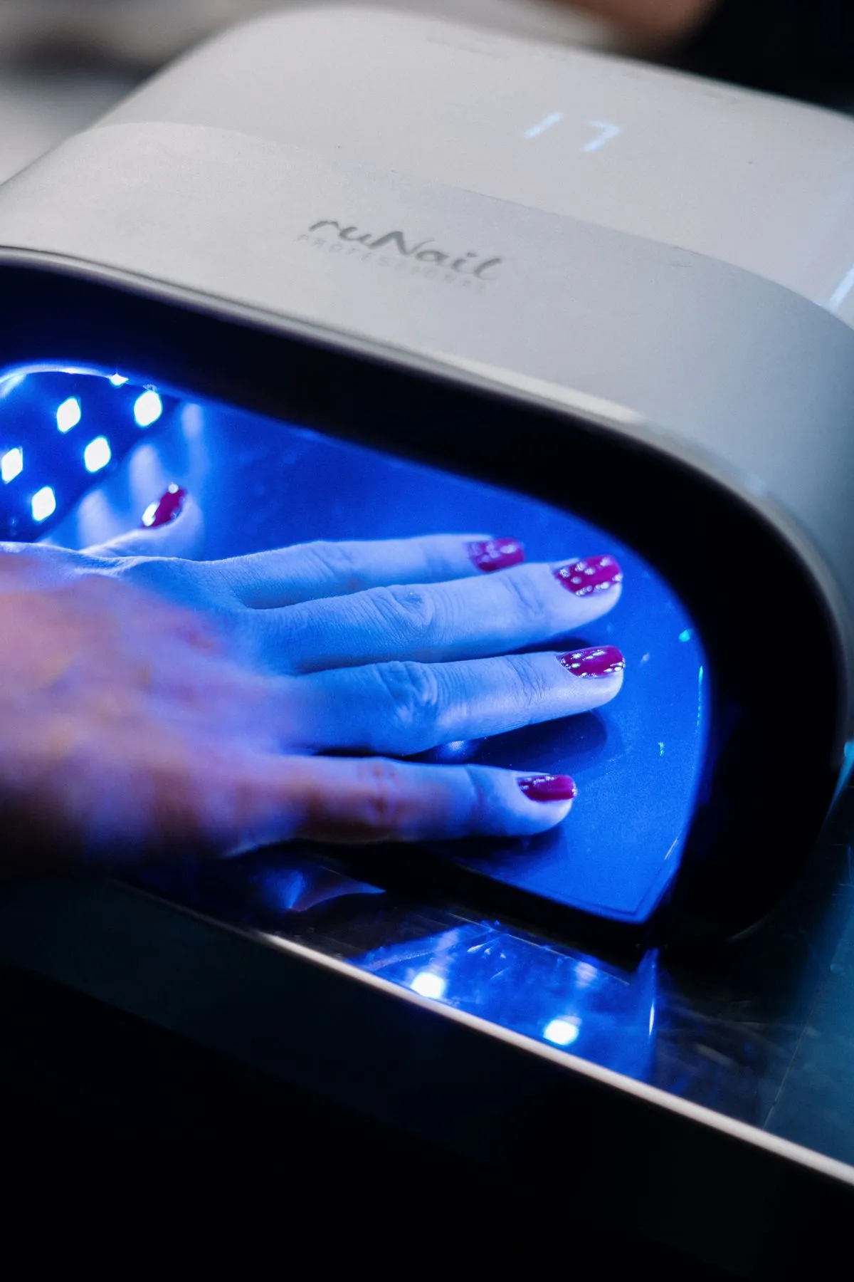 Mano con uñas esmaltadas secándose bajo una lámpara UV