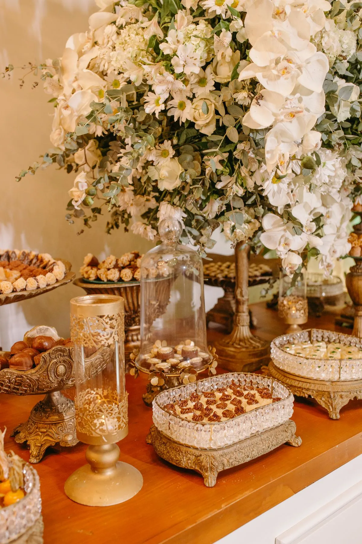 Mesa de dulces con bandejas doradas y arreglo de flores blancas