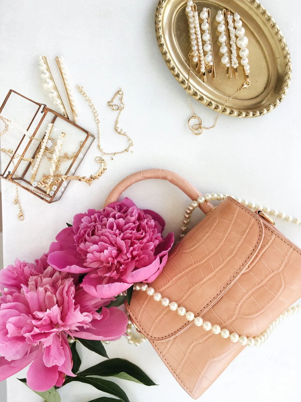 Cartera rosa con collar de perlas, aros y flores sobre fondo blanco