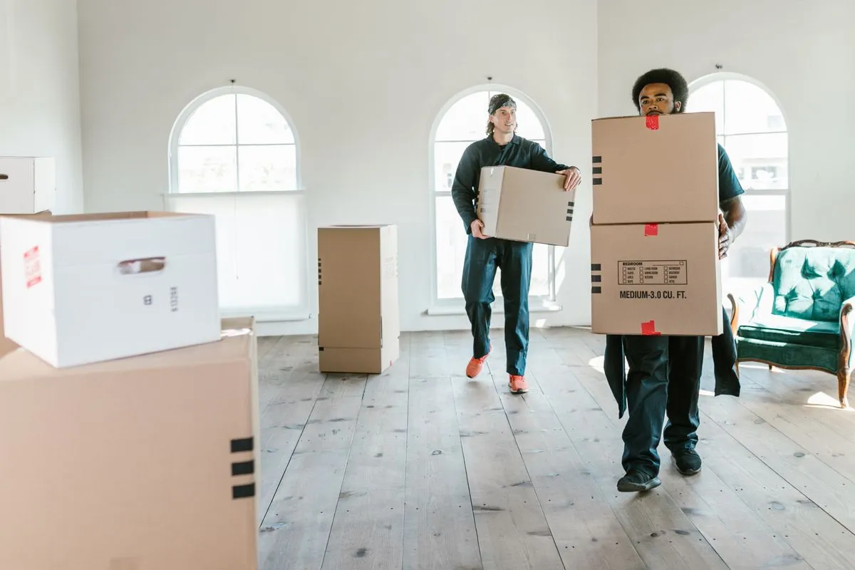 Dos ayudantes cargando cajas de mudanza dentro de una casa